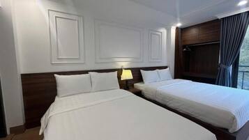 Habitación de hotel con dos camas, una mesita de noche con lámpara y una ventana con cortinas.