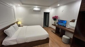 Hotellihuone, jossa on sänky, yöpöytä, lamppu, televisio ja pieni jakkara.