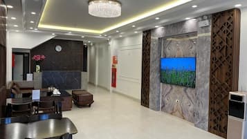 A modern lobby with a reception desk, seating area, and a large flat-screen TV mounted on a marble wall.