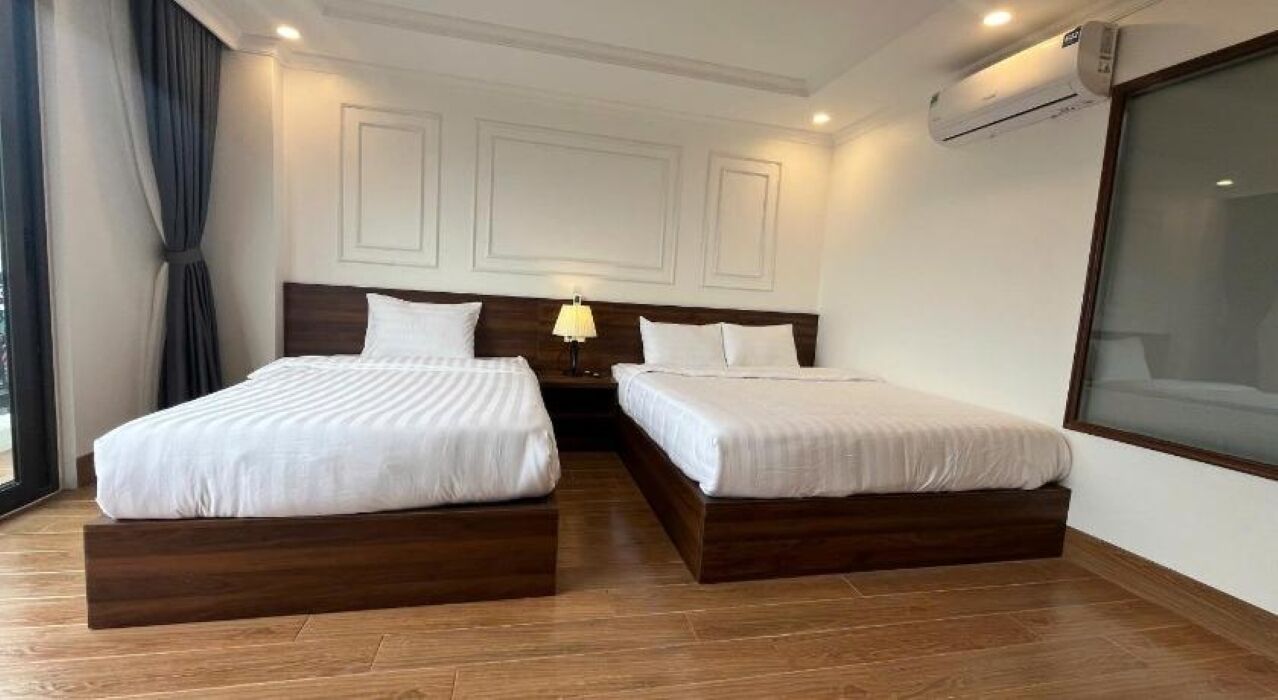 Habitación de hotel con dos camas, una mesita de noche con lámpara y un ventanal grande.