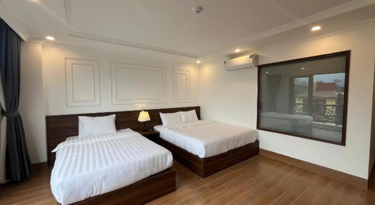 A hotel room with two beds, a large window, and a ceiling-mounted air conditioning unit.