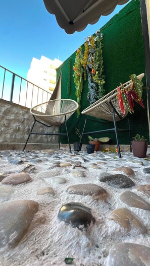 Eine Dachterrasse mit zwei Korbstühlen, Topfpflanzen und einer grünen Wand mit künstlicher Bepflanzung.