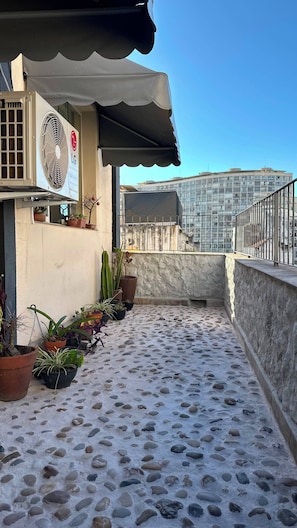 Terraço no telhado com plantas em vasos, um espelho d'água e vista para um edifício moderno.