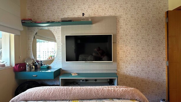 Ein Schlafzimmer mit einem Bett, einem Schminktisch, einem Spiegel, einem Fernseher und einem Fenster.