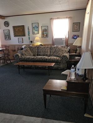 A living room with a sofa, a coffee table, a lamp, and a clock on the wall.