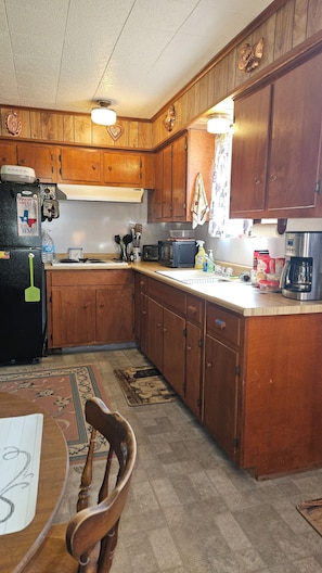 A kitchen with wooden cabinets, a refrigerator, a microwave, a coffee maker, and a dining table with chairs.