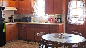 A compact kitchen with wooden cabinets, a dining table, and a refrigerator. - Cabin for A&M Games, Fishing or Family Get-a-Ways! (Somerville)