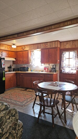 A compact kitchen with wooden cabinets, a dining table, and a refrigerator.