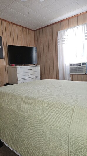 Une chambre avec un lit, un téléviseur posé sur une commode et un appareil de climatisation.