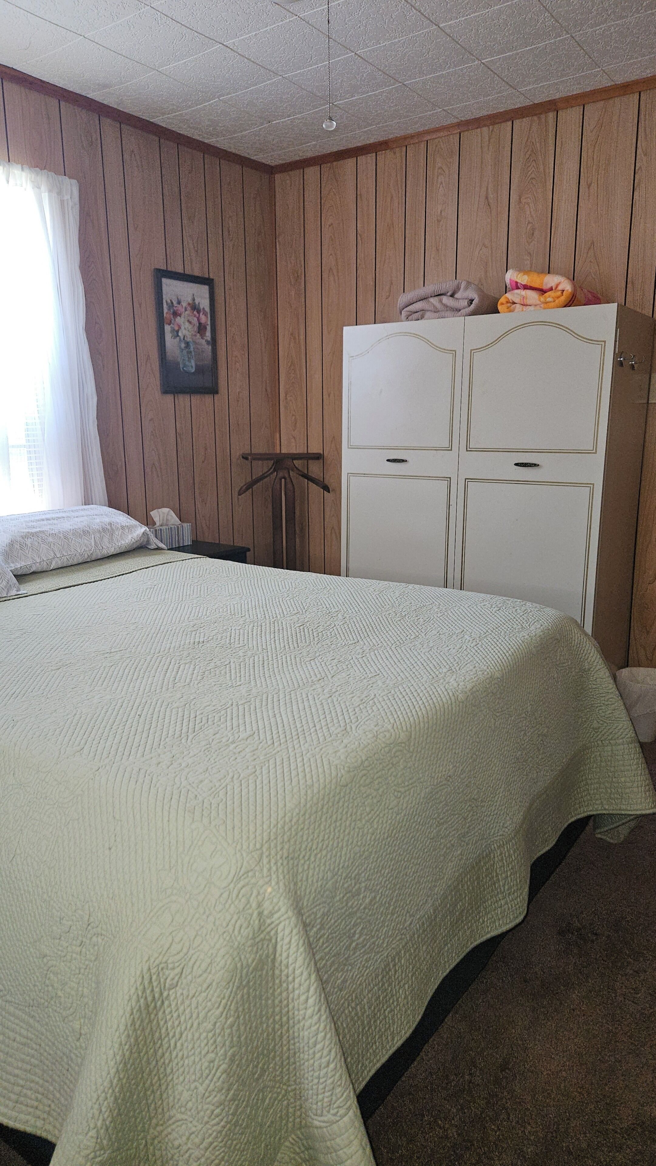 A bedroom with a bed, a wardrobe, a picture on the wall, and a window with curtains.