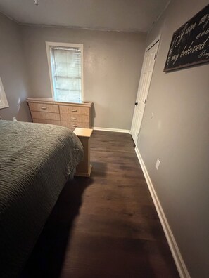 Un dormitorio con cama, cómoda, ventana y una pared con una cita.