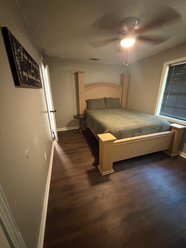A bedroom with a bed, a ceiling fan, a nightstand, and a window with blinds.