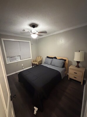 A bedroom with a bed, a chair, a nightstand, a lamp, and a ceiling fan.