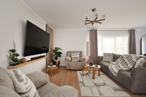 A modern living room with a flat-screen TV, a sofa, a chair, a coffee table, and a chandelier.