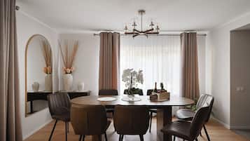 Un coin repas comprenant une table ronde, six chaises, un lustre et une vue sur l’extérieur grâce à de grandes fenêtres.