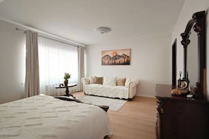 A bedroom with a bed, a sofa, a dresser, a painting, and a window with curtains.