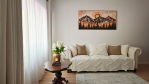 En stue med en sofa, et bord med en vase blomster, og et billede af bjerge på væggen.