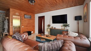 En moderne stue med træloft, stort fladskærms-tv, sofa og sofabord.