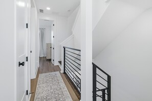 A hallway with white walls, a wooden floor, and a patterned rug. - Luxury 3BR Waterfront w/ Private Rooftop Skyline Views (Jacksonville)
