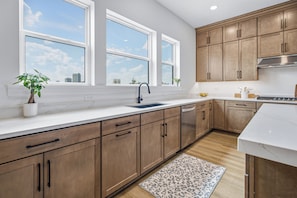 A modern kitchen with wooden cabinets, a white countertop, a sink, and a window with a city view. - Luxury 3BR Waterfront w/ Private Rooftop Skyline Views (Jacksonville)