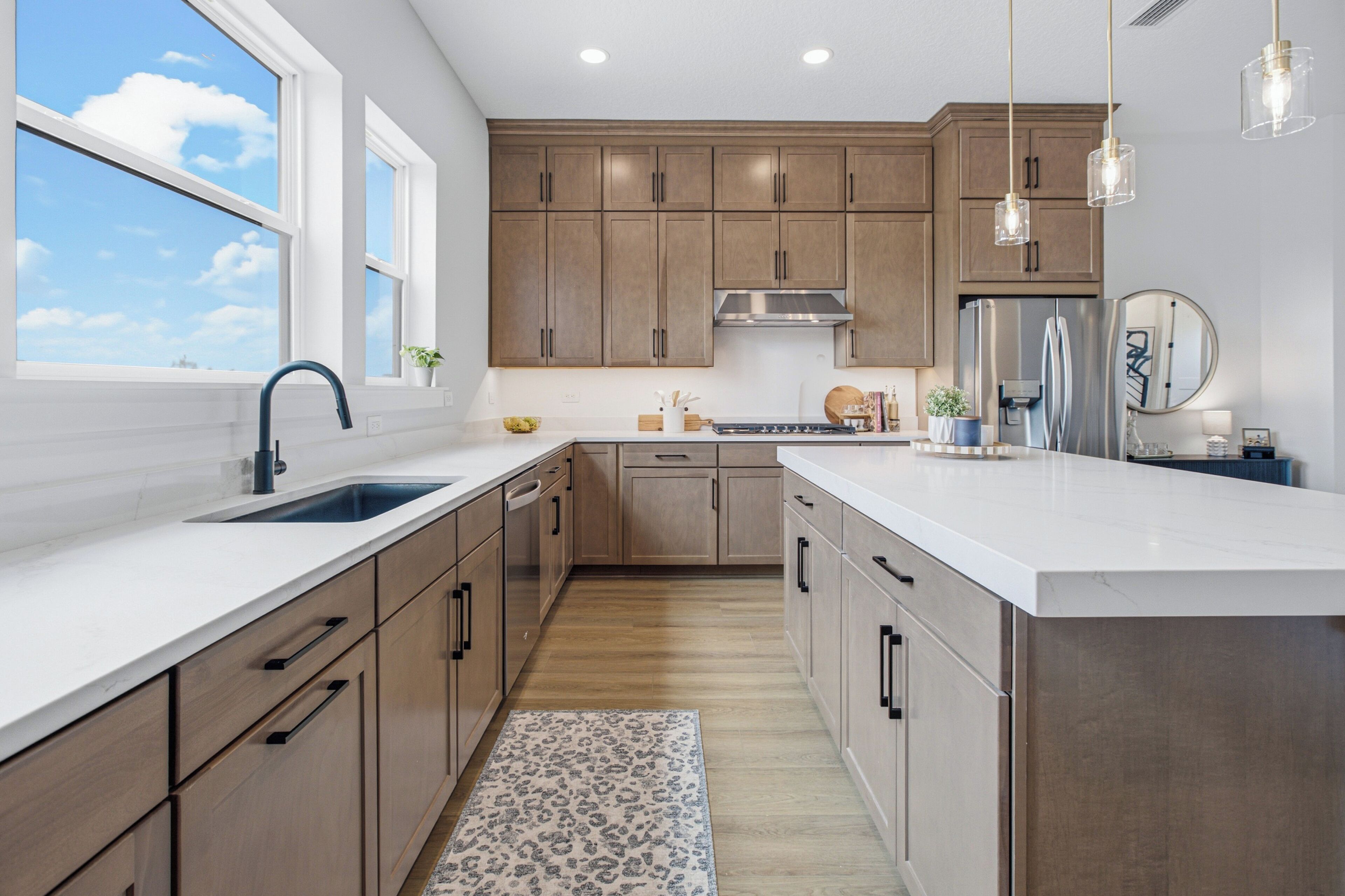 A modern kitchen with wooden cabinets, a stainless steel refrigerator, and a large window.