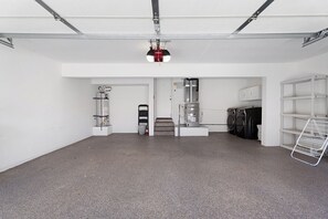 Een nette, industrieel ingerichte kamer met een betonnen vloer, een aan het plafond gemonteerde projector, een boiler en een wasruimte met wasmachines.