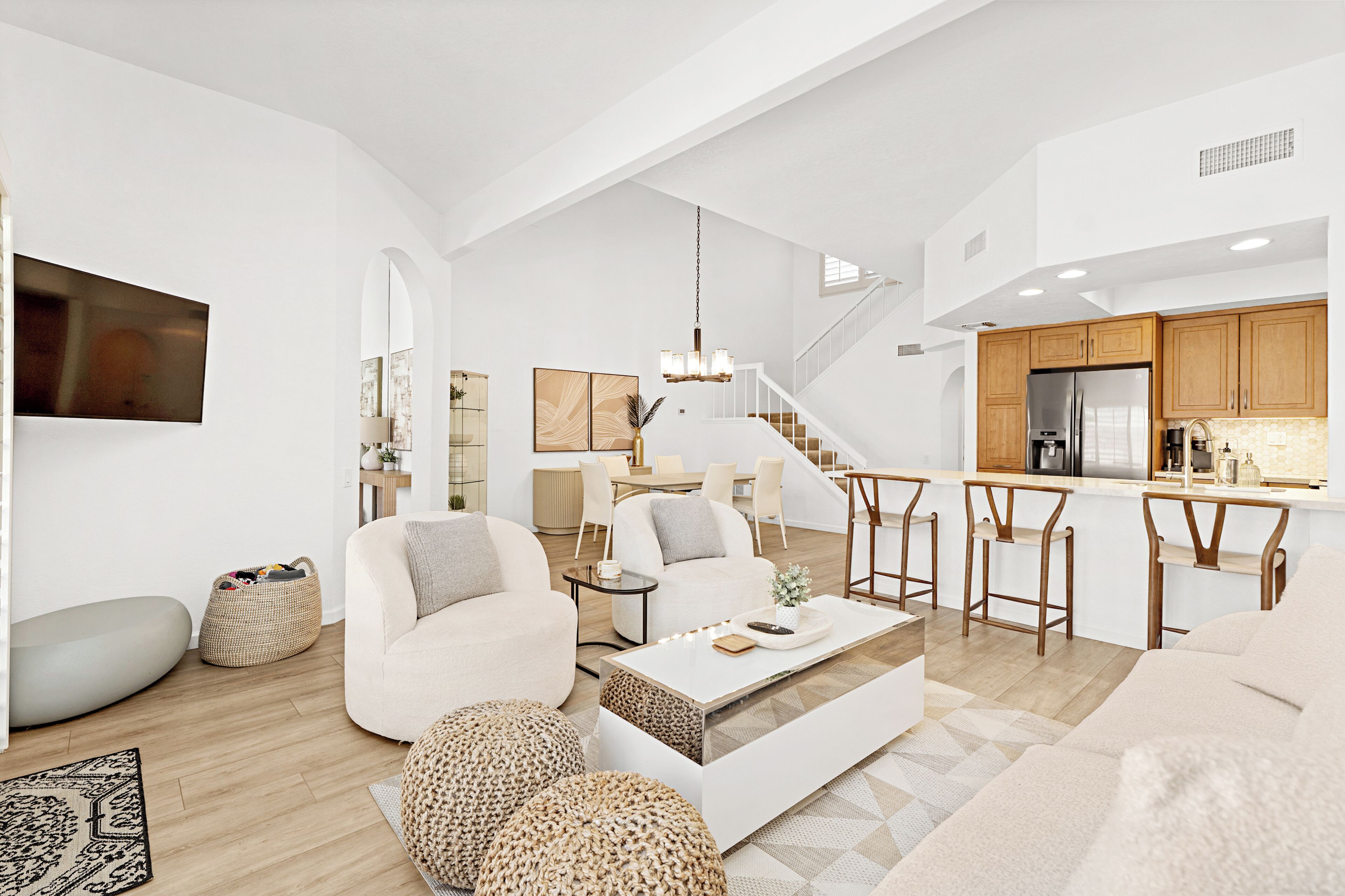 A spacious living area with a sofa, coffee table, and ottomans, a dining area with chairs, and a kitchen with a refrigerator and stove.