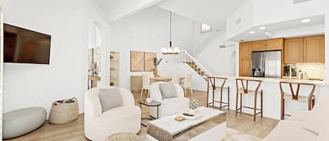 A spacious living area with a sofa, coffee table, and ottomans, a dining area with chairs, and a kitchen with a refrigerator and stove.