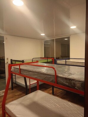 A dormitory room with bunk beds, a large mirror, and a door leading to another room.