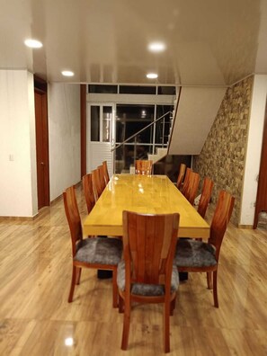 A dining area with a long wooden table and chairs, a staircase, and a stone wall.