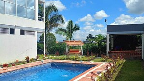 A modern building with a swimming pool, a covered seating area, and a well-maintained garden.
