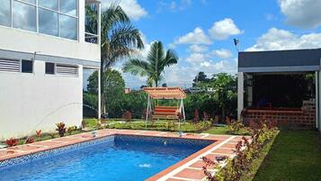 A modern building with a swimming pool, a covered seating area, and a well-maintained garden.
