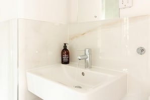 Un lavamanos blanco con salpicadero de mármol, una botella de champú de la colección del hotel y un grifo.