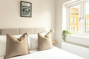 A hotel room with a bed, two pillows, a framed picture on the wall, a bedside table with a lamp, and a window with a view of buildings. - Guestready - Fownes Street (Dublin)
