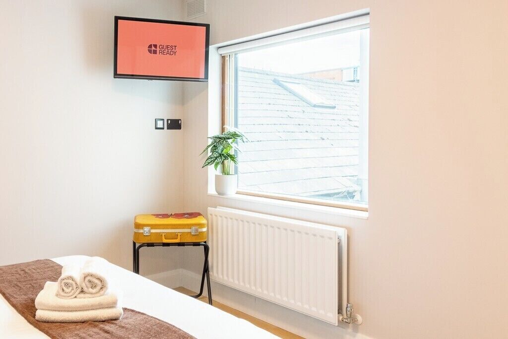 Ein Hotelzimmer mit einem Bett, einem Heizkörper, einem Fenster mit Aussicht, einer Pflanze und einem gerahmten Bild an der Wand.