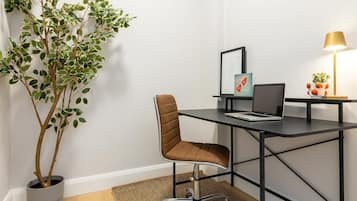 Ein moderner Arbeitsplatz mit Schreibtisch, Stuhl, Laptop, gerahmtem Kunstwerk und Topfpflanze.