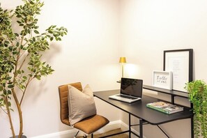 Un espacio de oficina moderno con escritorio, laptop, silla, lámpara, cuadro enmarco y planta en maceta.