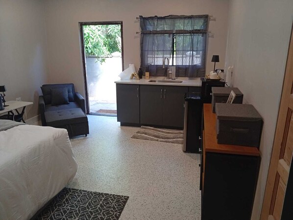 A compact room with a bed, a sofa, a kitchenette, and a window with a view of greenery. - Modern & Roomy 4BR/3.5BA Gateway to Port of Spain Fully Air-Conditioned (Morvant)