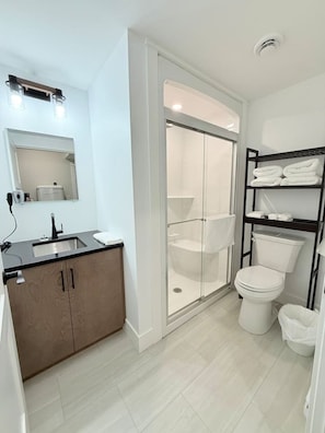 Un bagno moderno con box doccia in vetro, un water e un lavabo con mobiletto in legno.