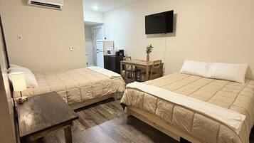 Ein Zimmer mit zwei Betten, einem Tisch, einem Stuhl, einem Fernseher und einer Klimaanlage.