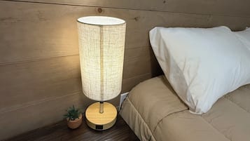 Une table de chevet en bois avec une lampe, une petite plante en pot et un lit avec une literie blanche.