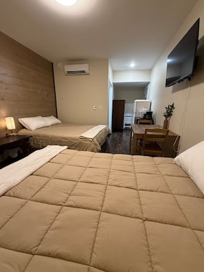 Una habitación de hotel con dos camas, un escritorio, una silla, un televisor y un equipo de aire acondicionado.