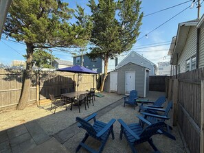 Ein Garten mit einem Holztisch und -stühlen, einem blauen Adirondack-Sessel, einer kleinen Gartenhütte und einem Holzzaun.
