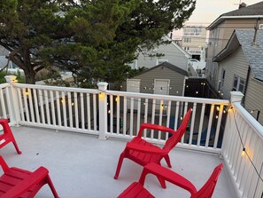 Ein Balkon mit weißen Geländern, Lichterketten und roten Plastikstühlen.