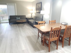 A living room with a sofa, two side tables with lamps, a wooden dining table with chairs, and a large window with blinds. - The "Merlot" - Updated Condo - DISCOUNT 4+ nights! (Branson)