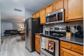 A modern kitchen with stainless steel appliances, wooden cabinets, and a dining area with a sofa and table. - The Merlot at The Vinyards: View, Pool, and Fun! (Branson)