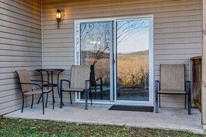 A covered patio with a sliding glass door, two chairs, a small table, and a wall-mounted light fixture. - The Merlot at The Vinyards: View, Pool, and Fun! (Branson)