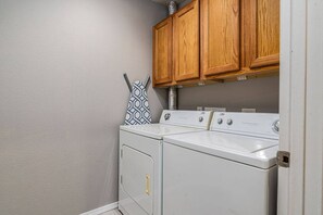 Une buanderie équipée de deux machines à laver et deux sèche-linge superposés, avec des armoires en bois au-dessus et une serviette à motifs accrochée au mur.