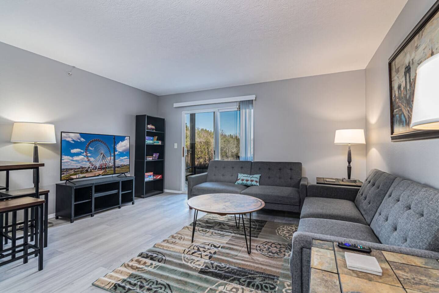 A living room with a sofa, coffee table, TV, bookshelf, and a window with a view.