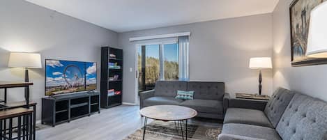 A living room with a sofa, coffee table, TV, bookshelf, and a window with a view.